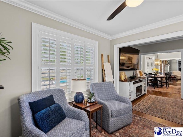 living area with a ceiling fan, ornamental molding, and wood finished floors