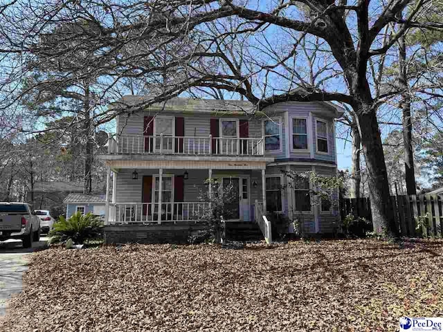 view of front facade featuring a balcony, a porch, and fence