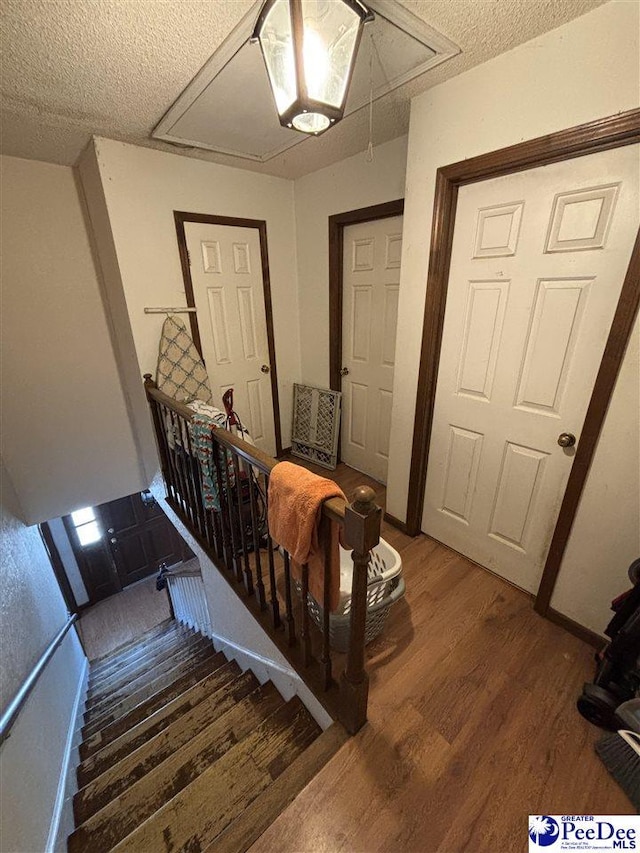 stairs featuring a textured ceiling, attic access, and wood finished floors