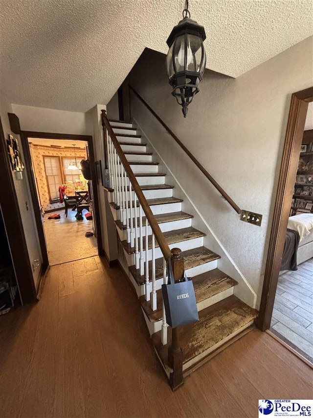 staircase with hardwood / wood-style floors, a textured wall, baseboards, and a textured ceiling