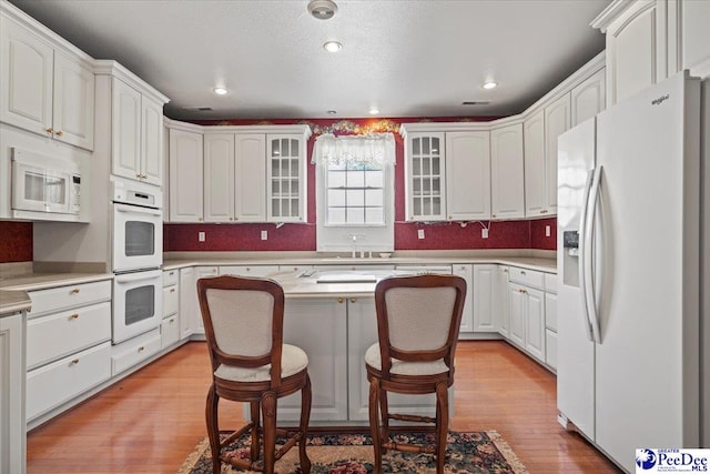 kitchen featuring white appliances, a breakfast bar, white cabinets, and a kitchen island