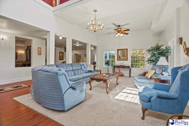 living room with wood-type flooring, ceiling fan with notable chandelier, and a high ceiling