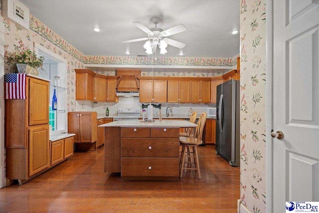 kitchen with dark hardwood / wood-style flooring, stainless steel fridge, a kitchen breakfast bar, range with electric cooktop, and a kitchen island with sink