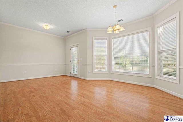 spare room featuring ornamental molding, light wood finished floors, visible vents, and an inviting chandelier