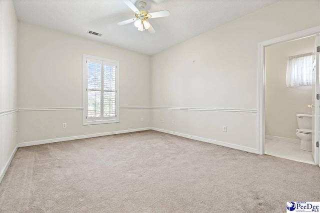 unfurnished bedroom featuring a textured ceiling, ensuite bathroom, light carpet, visible vents, and baseboards