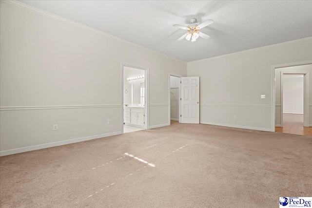 unfurnished bedroom featuring baseboards, ornamental molding, ensuite bath, and light colored carpet