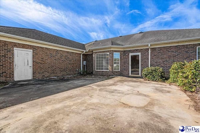 rear view of property with brick siding, a shingled roof, and a patio