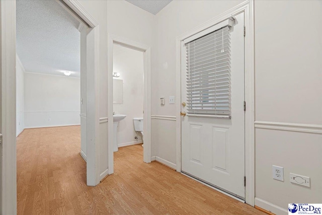 hall featuring light wood-style floors, baseboards, and a textured ceiling