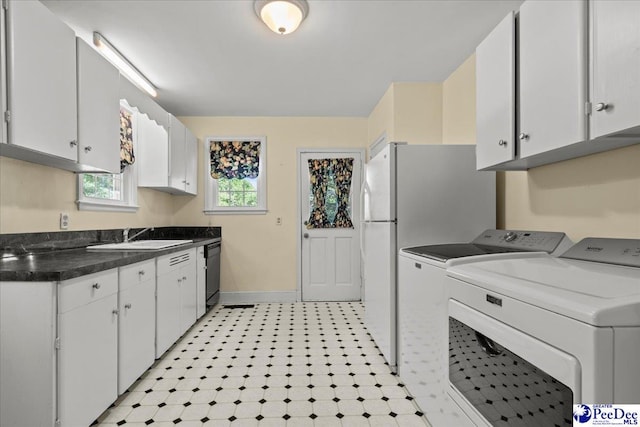 kitchen featuring washing machine and clothes dryer, dark countertops, a sink, dishwasher, and white cabinetry