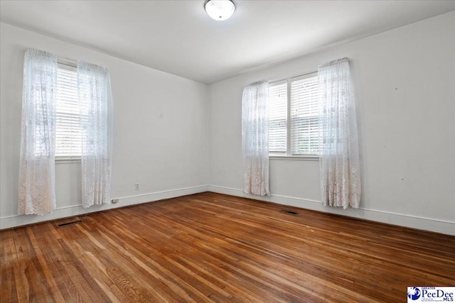 spare room with wood finished floors, visible vents, and plenty of natural light