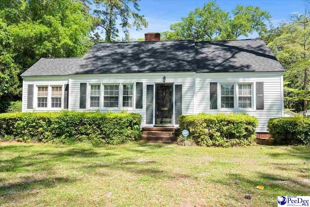 view of front of house featuring a chimney, a front lawn, and a shingled roof