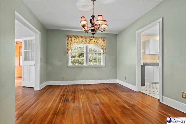 unfurnished dining area with baseboards, a chandelier, and hardwood / wood-style floors