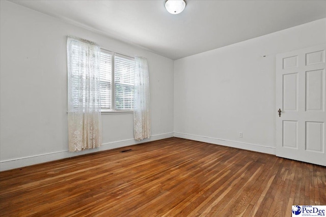 empty room featuring wood finished floors, visible vents, and baseboards