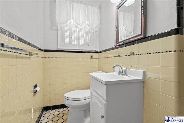 bathroom featuring tile patterned floors, a wainscoted wall, toilet, tile walls, and vanity