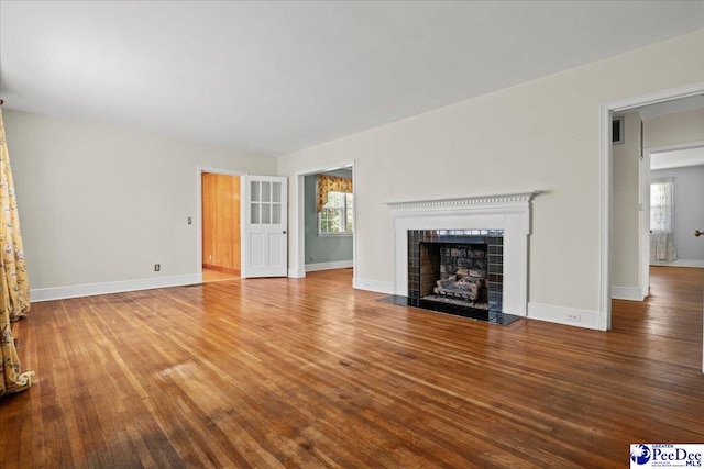 unfurnished living room with a fireplace, wood finished floors, visible vents, and baseboards