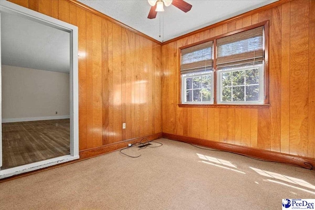 empty room featuring wood walls, a ceiling fan, carpet floors, crown molding, and baseboards