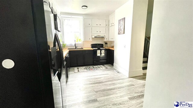 kitchen featuring sink, white cabinetry, wooden counters, light hardwood / wood-style floors, and black appliances