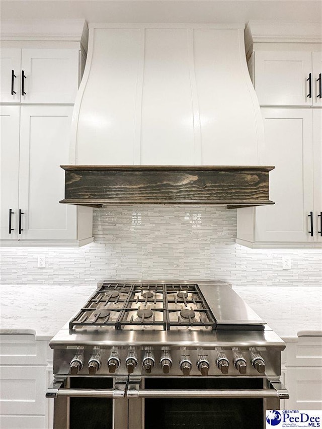 kitchen featuring backsplash, double oven range, white cabinetry, light stone countertops, and premium range hood