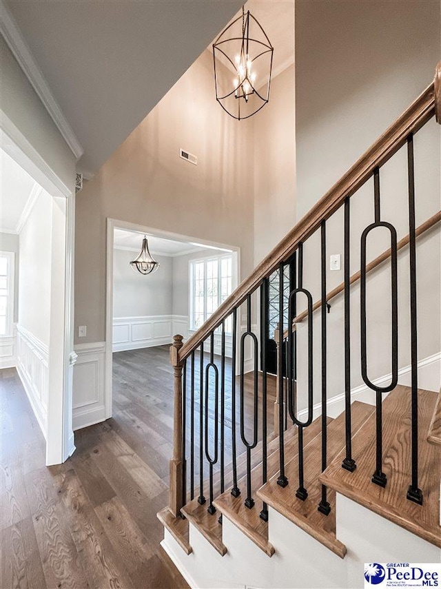 stairway with a notable chandelier, crown molding, a decorative wall, and wood finished floors