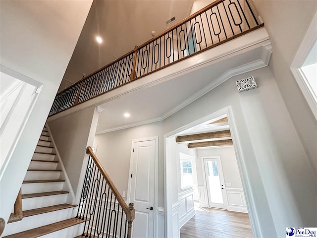 staircase with visible vents, wood finished floors, a high ceiling, a decorative wall, and beam ceiling