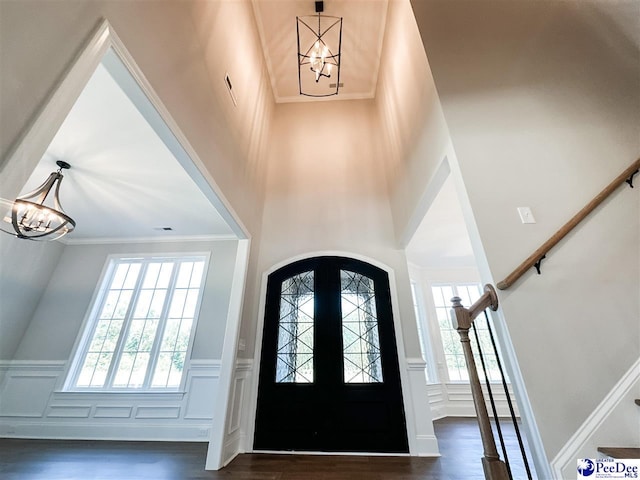 entrance foyer with arched walkways, dark wood-style flooring, stairs, french doors, and a chandelier