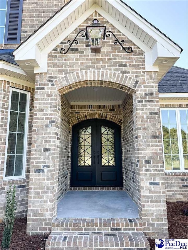 entrance to property with a shingled roof, french doors, and brick siding