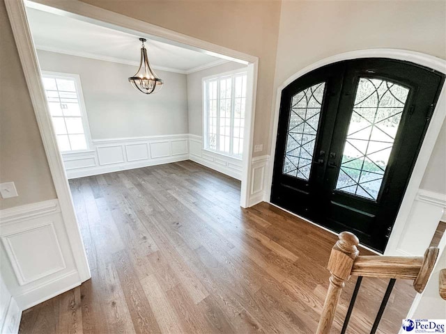 entrance foyer with arched walkways, a wainscoted wall, ornamental molding, wood finished floors, and a chandelier