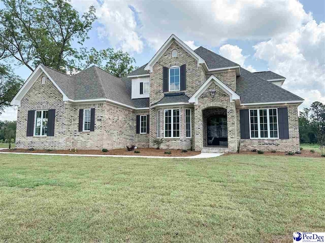 craftsman-style home with roof with shingles, a front yard, and brick siding