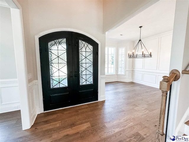 entryway with french doors, a decorative wall, an inviting chandelier, and wood finished floors