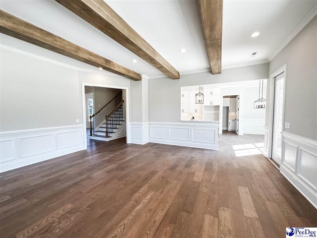 unfurnished living room with beam ceiling, a decorative wall, dark wood-style flooring, and stairs