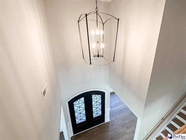 entryway with arched walkways, dark wood-type flooring, an inviting chandelier, stairs, and french doors