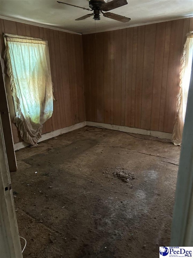 spare room with a ceiling fan, a wealth of natural light, and wood walls