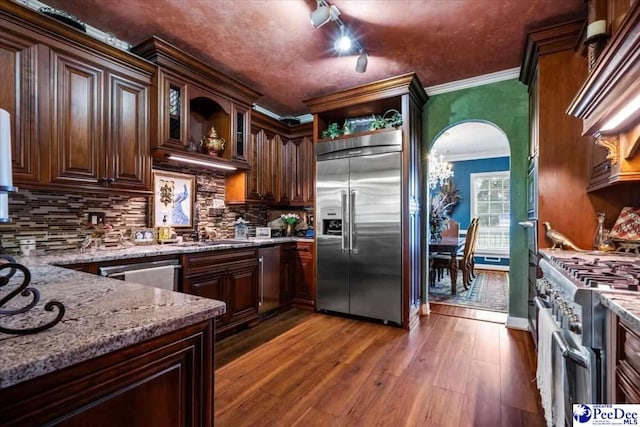 kitchen with crown molding, dark hardwood / wood-style floors, high end appliances, light stone counters, and decorative backsplash