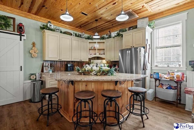 kitchen with light stone counters, cream cabinetry, a kitchen island, and pendant lighting