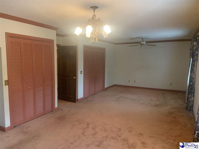 unfurnished bedroom with a notable chandelier, carpet, a textured ceiling, baseboards, and ornamental molding