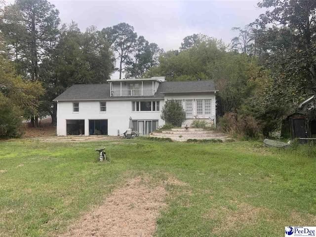 rear view of house with a lawn, an attached garage, and stucco siding