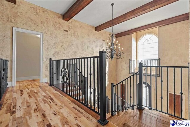 stairway featuring beam ceiling, hardwood / wood-style flooring, and a chandelier