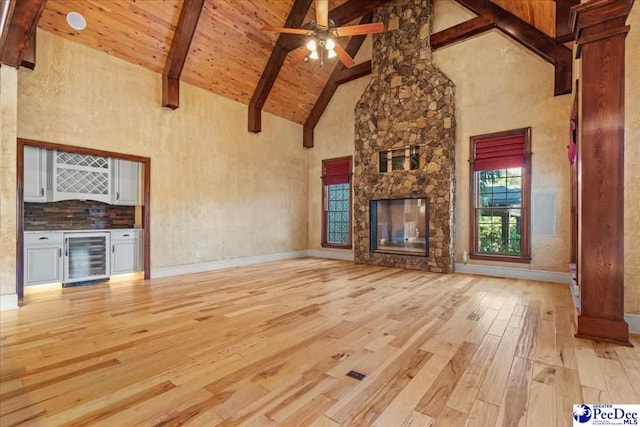 unfurnished living room with a fireplace, wine cooler, light hardwood / wood-style floors, bar area, and beam ceiling