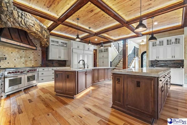 kitchen featuring pendant lighting, custom range hood, range with two ovens, and a center island with sink