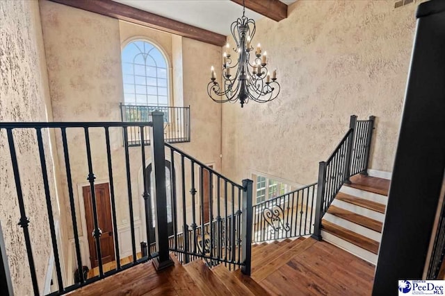 stairs with beamed ceiling, plenty of natural light, hardwood / wood-style floors, and an inviting chandelier