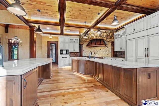 kitchen with white cabinetry, a spacious island, light stone countertops, and hanging light fixtures