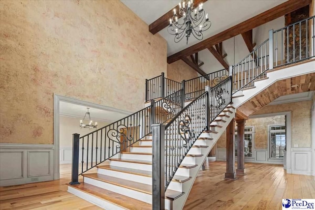 stairs with beamed ceiling, a towering ceiling, hardwood / wood-style floors, and a notable chandelier