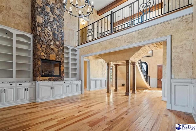 unfurnished living room featuring an inviting chandelier, built in shelves, a towering ceiling, and light wood-type flooring