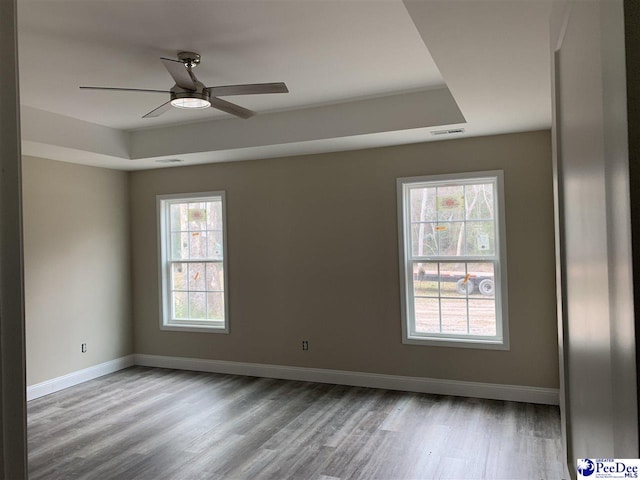 spare room with ceiling fan, light wood-type flooring, and a tray ceiling