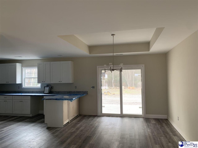 kitchen featuring pendant lighting, white cabinetry, a notable chandelier, dark hardwood / wood-style flooring, and a raised ceiling