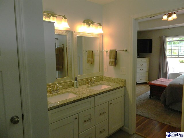 ensuite bathroom featuring wood finished floors, a sink, and double vanity