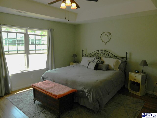 bedroom with wood finished floors, visible vents, a ceiling fan, and baseboards