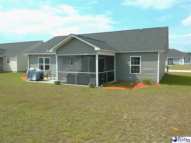 back of house with a lawn, a sunroom, a patio, and a shingled roof