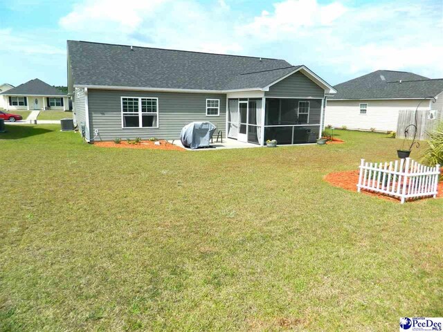 back of house featuring cooling unit, a sunroom, roof with shingles, and a lawn