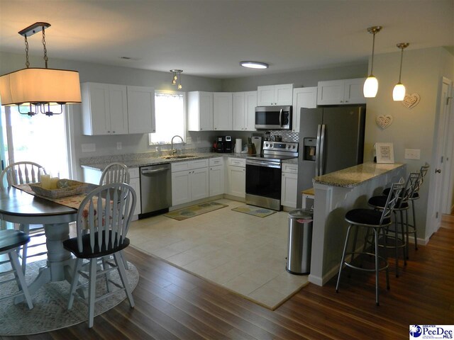 kitchen featuring white cabinets, stainless steel appliances, a peninsula, a sink, and light stone counters